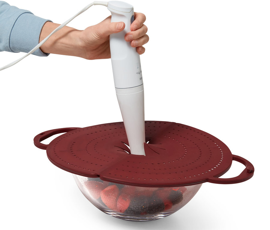 Eine Hand hält einen weißen Stabmixer über eine Schüssel mit Früchten, die mit einem 4-in-1-Pfannen-Spritzschutz abgedeckt ist.