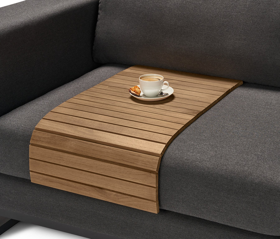 Ein Teak-Sofatablett mit flexiblen Lamellen liegt auf einem grauen Sofa. Auf dem Tablett stehen eine Tasse Kaffee und ein Keks.