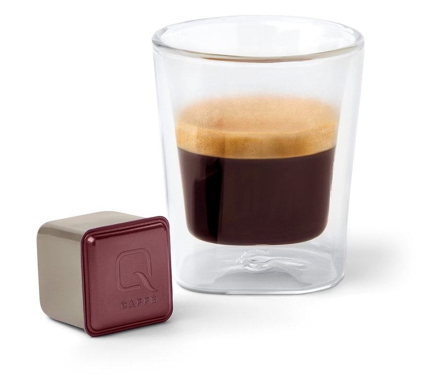 Eine Qbo Caffè KINYAA GALERAS Kapsel steht neben einem Glas Kaffee.