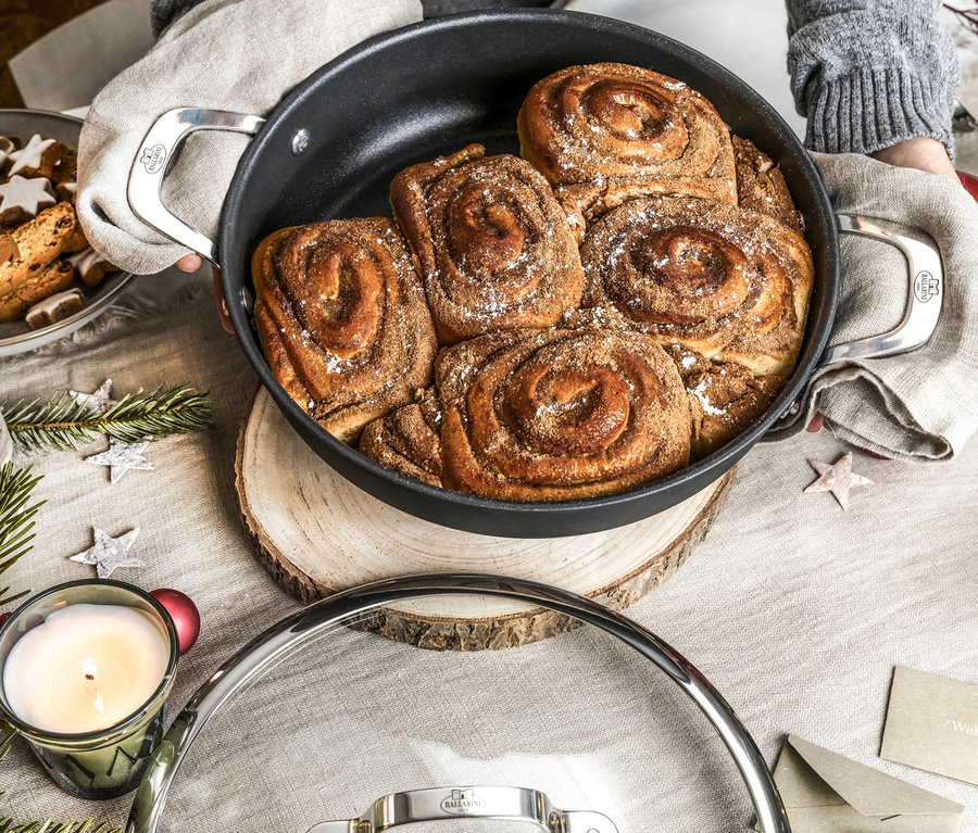 Person hält Ballarini Alba Servierpfanne, 28 cm, voll mit Zimtschnecken.