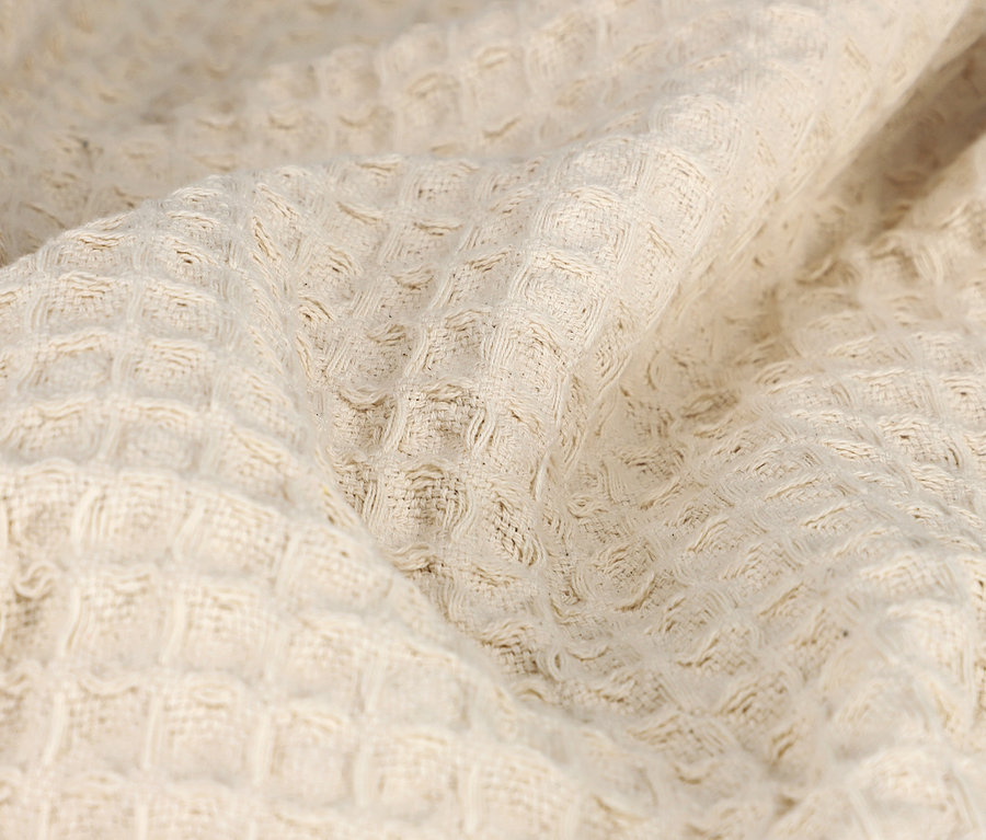 Nahaufnahme einer cremefarbenen Wohndecke mit Waffelstruktur.