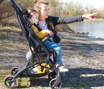 Eine Frau zeigt auf einen See, während sie ein Kind in einem schwarzen Osann Sportwagen »Vegas« schiebt.