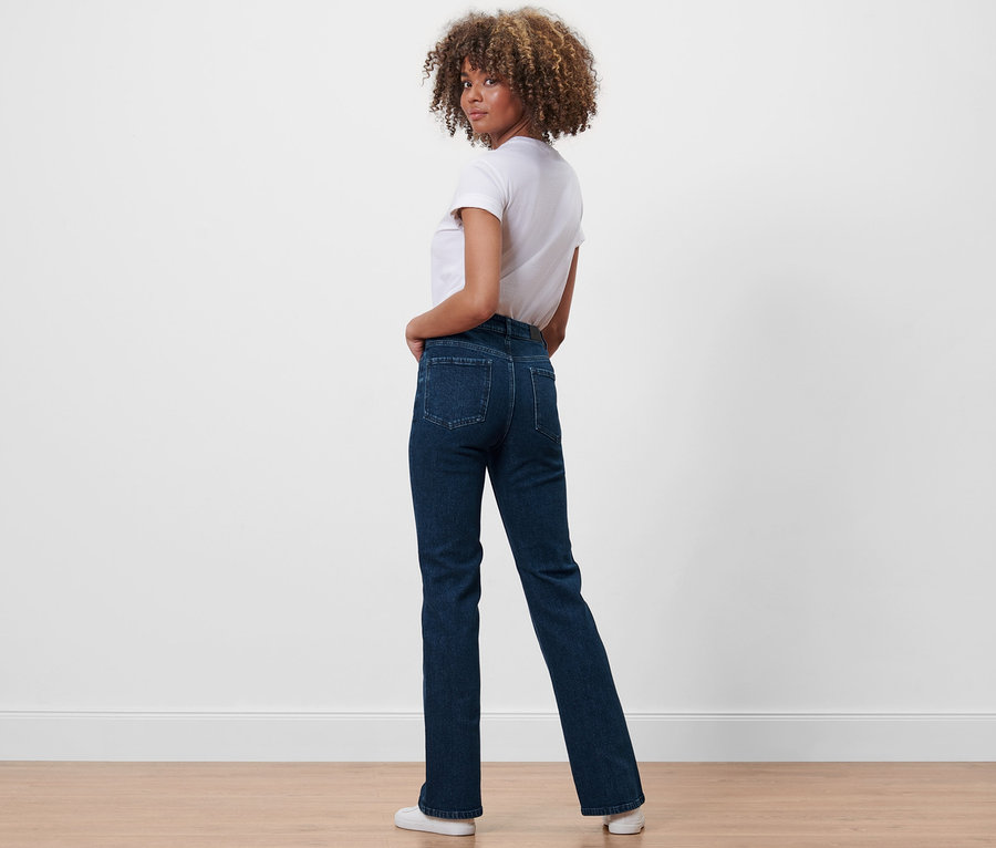 Frau blickt über die Schulter und posiert in Bootcut-Denim »Fit Lou« und weißem T-Shirt.