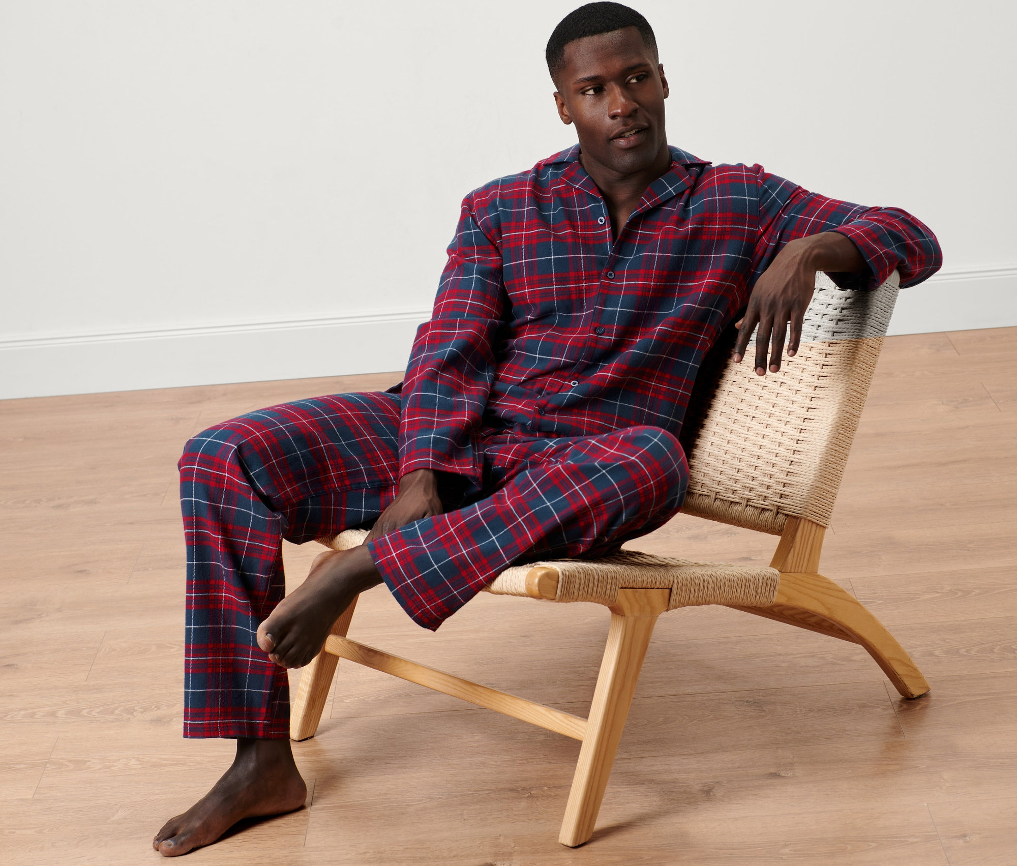 Mann sitzt in einem Stuhl und trägt einen blau-bordeauxroten Flanell-Pyjama.