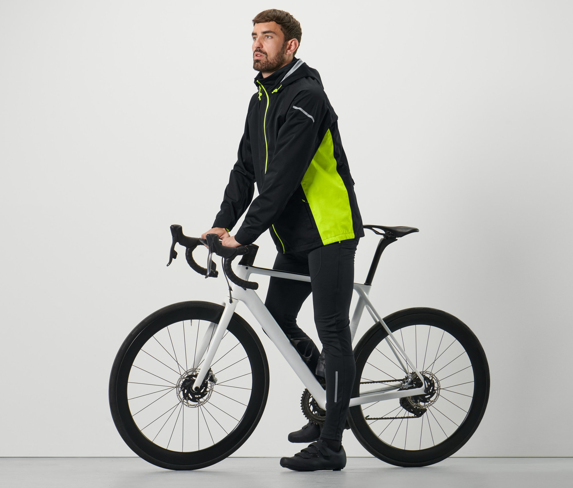 Mann posiert auf einem Fahrrad in einer schwarz-neongelben Rad-Regenjacke.