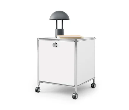 Ein weißer Beistelltisch mit Schublade Metall »CN3« mit einer grauen Lampe und einem Buch darauf.