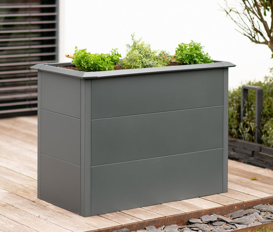 Ein graues Hochbeet mit Schneckenschutz und Bepflanzung steht auf einer Holzterrasse.