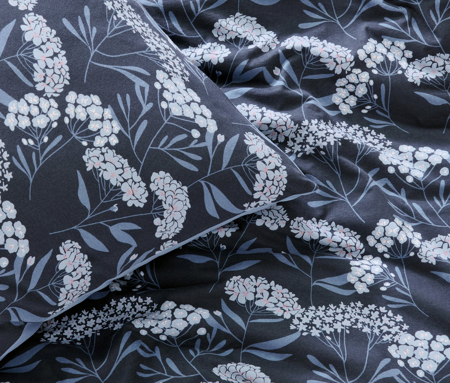 Nahaufnahme von marineblauer Winterjersey-Bettwäsche mit weißen Blüten und blauen Blättern.