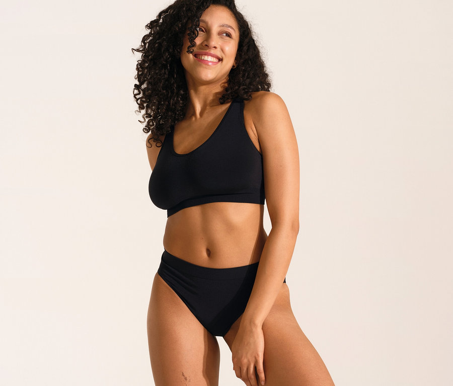 Lächelnde Frau posiert in schwarzem SCHIESSER Soft BH mit Pads und schwarzem SCHIESSER Rio Slip.