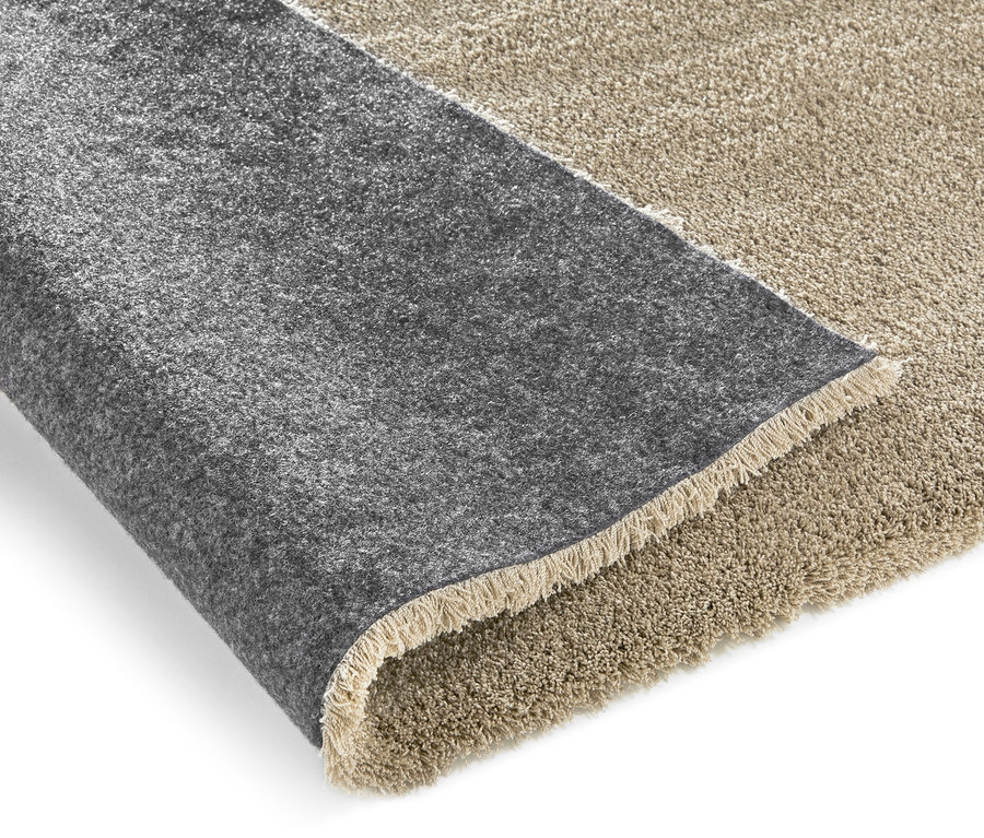Detailansicht eines beigen »Mellow« Teppichs mit kurzem Flor, teilweise aufgerollt, wobei die graue Unterseite sichtbar ist.