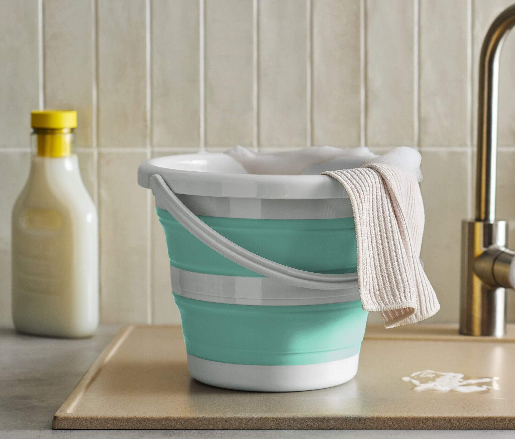 Ein faltbarer Putzeimer mit Lappen steht neben einem Spülbecken.
