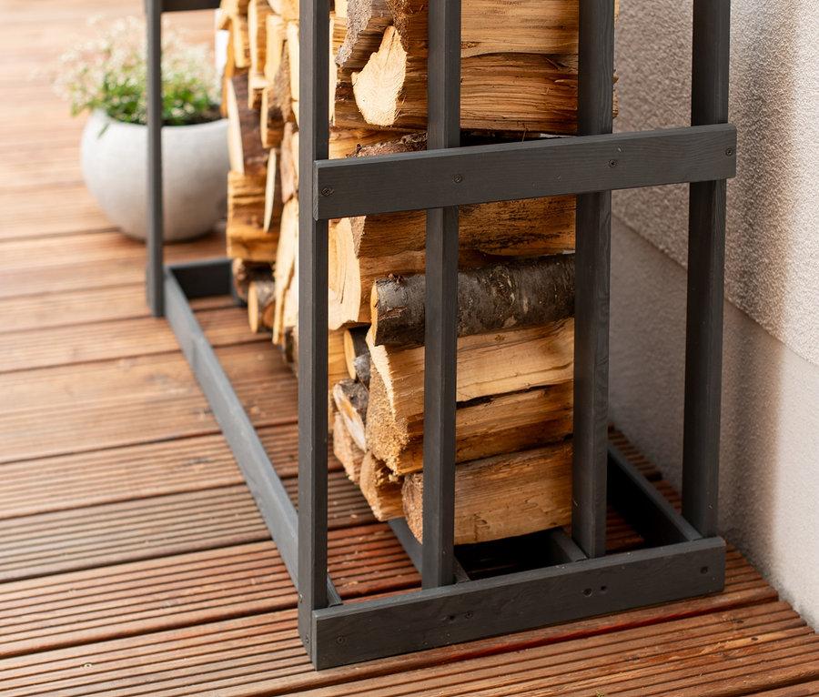 Ein mit Holzscheiten gefülltes Kaminholzregal »Harald« steht auf einer Holzterrasse an einer Hauswand.
