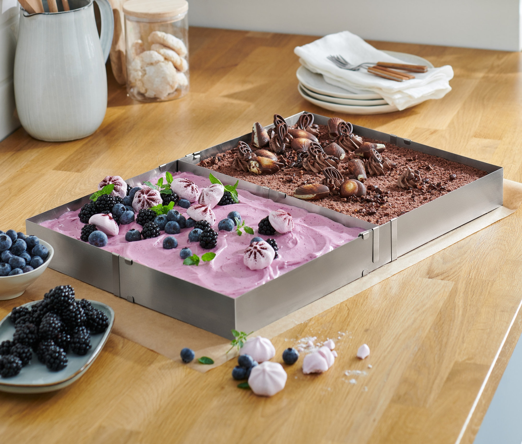 Zwei Edelstahl-Backrahmen mit Obst- und Schokoladenkuchen auf einer Holzplatte.