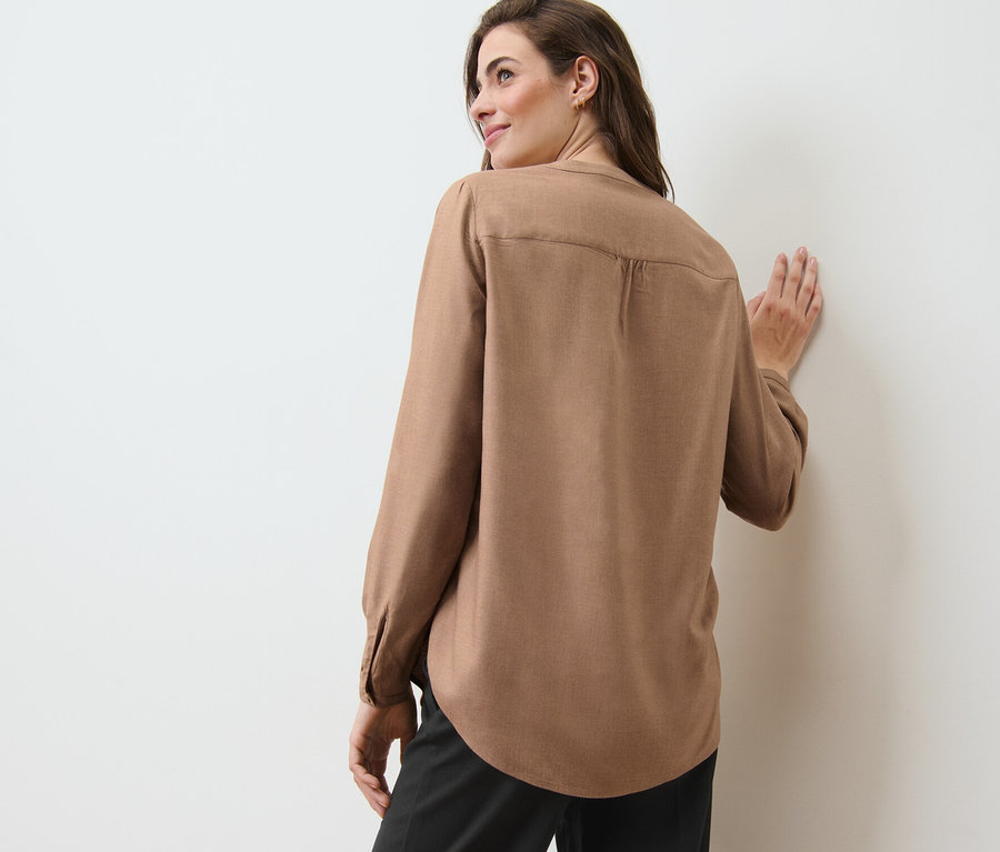 Frau lehnt in Tunikabluse an Wand.