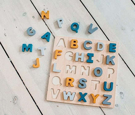 ABC-Puzzle »Caspar« mit verschiedenfarbigen Buchstaben auf weißem Holzhintergrund.