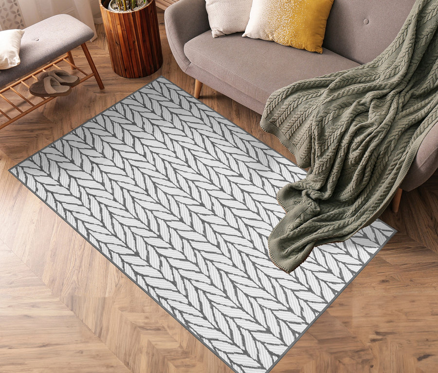 Grauer Outdoor-Wendeppich »Knitted Joy« liegt auf Holzboden neben einem Sofa.