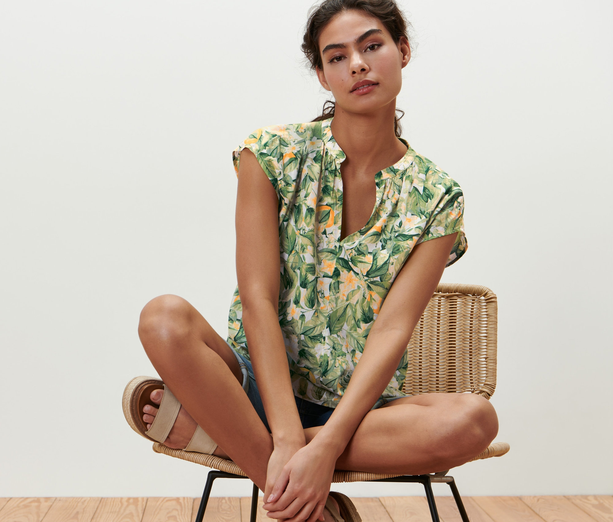 Frau sitzt auf einem Stuhl und trägt eine bedruckte Kurzarmbluse.