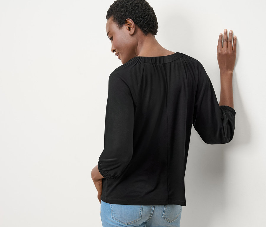 Frau von hinten trägt ein Blusenshirt mit Raffung und Jeans.