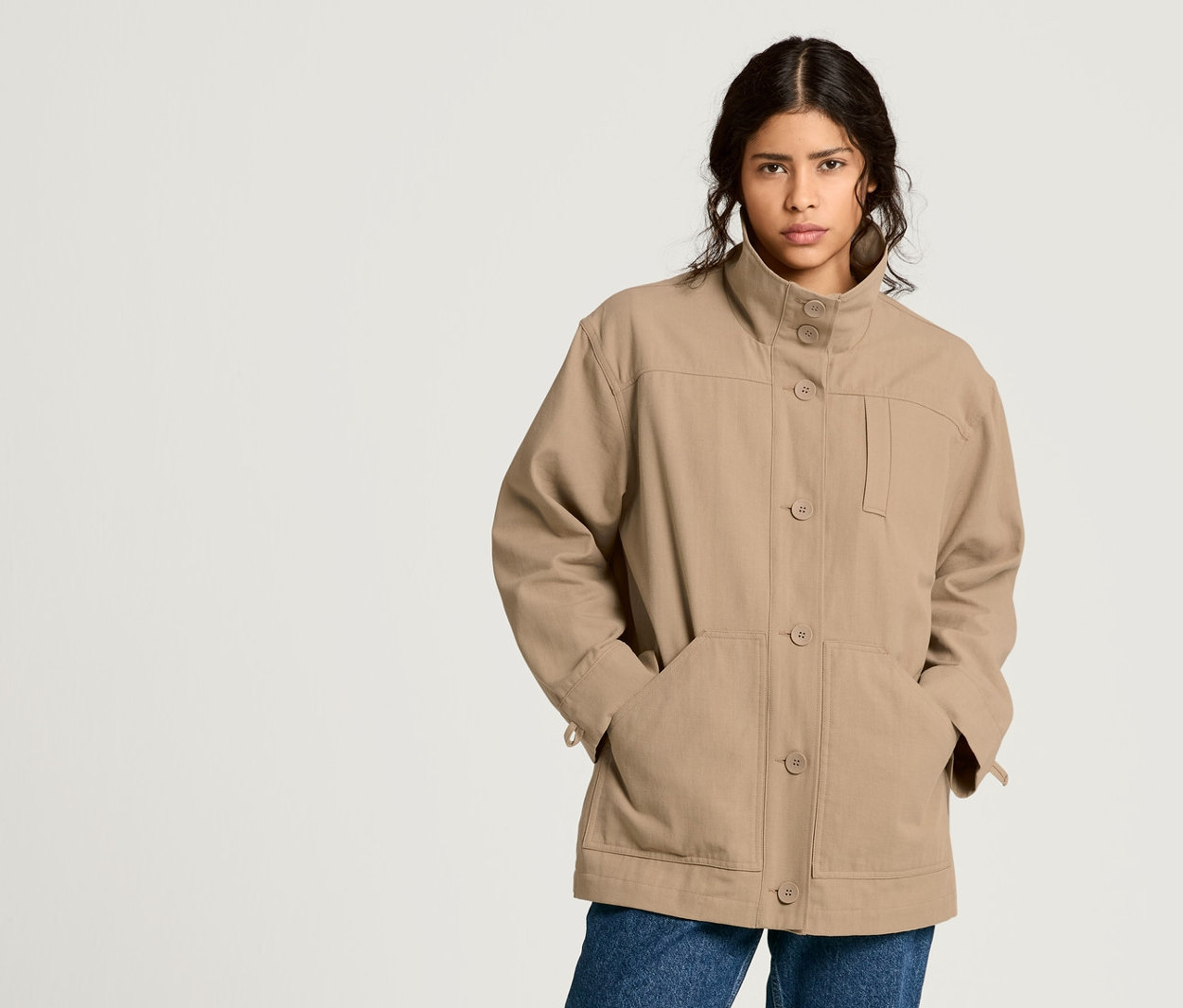 Frau posiert in NAH/STUDIO Parka aus recycelter Baumwolle, Mom-Jeans und Bluse.