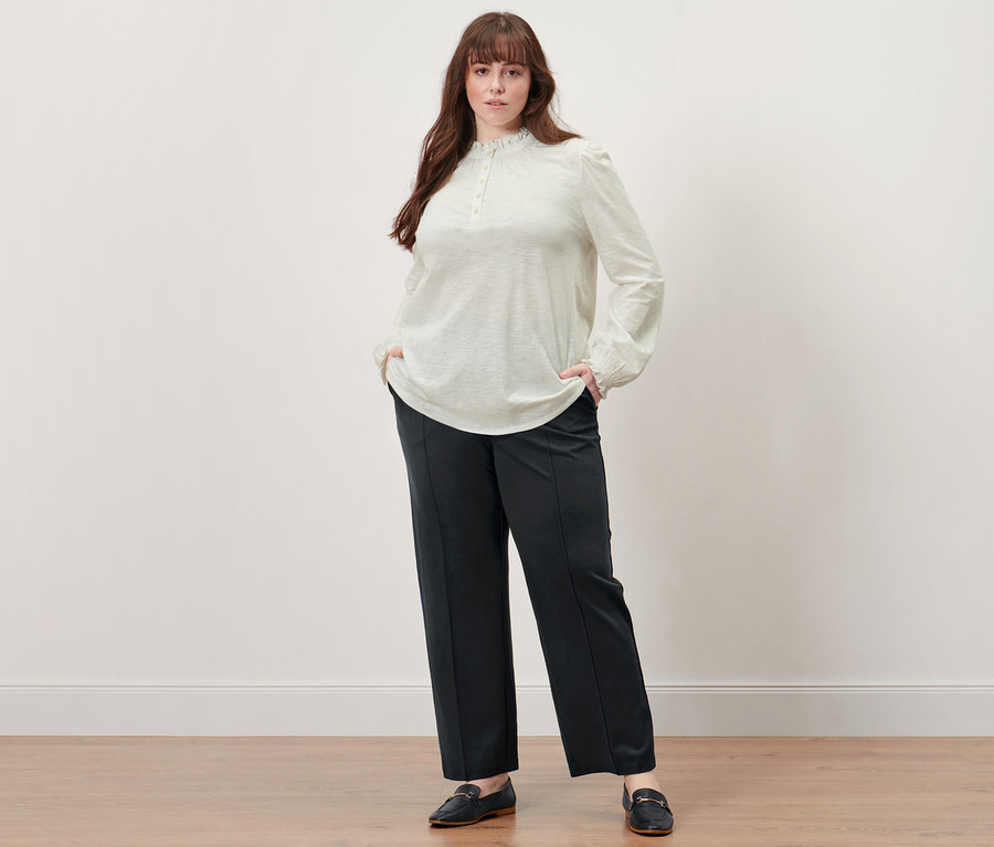 Frau posiert in Langarmshirt mit Rüschen und schwarzer Jerseyhose mit Biese.