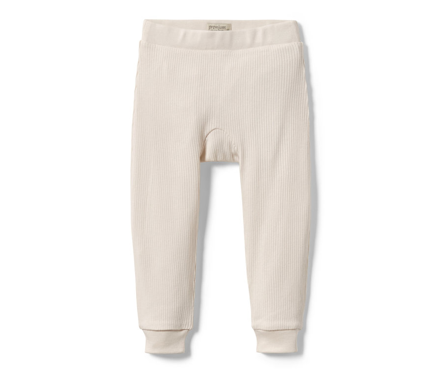 Eine hellbeige Baby-Strickhose liegt auf einem weißen Hintergrund.