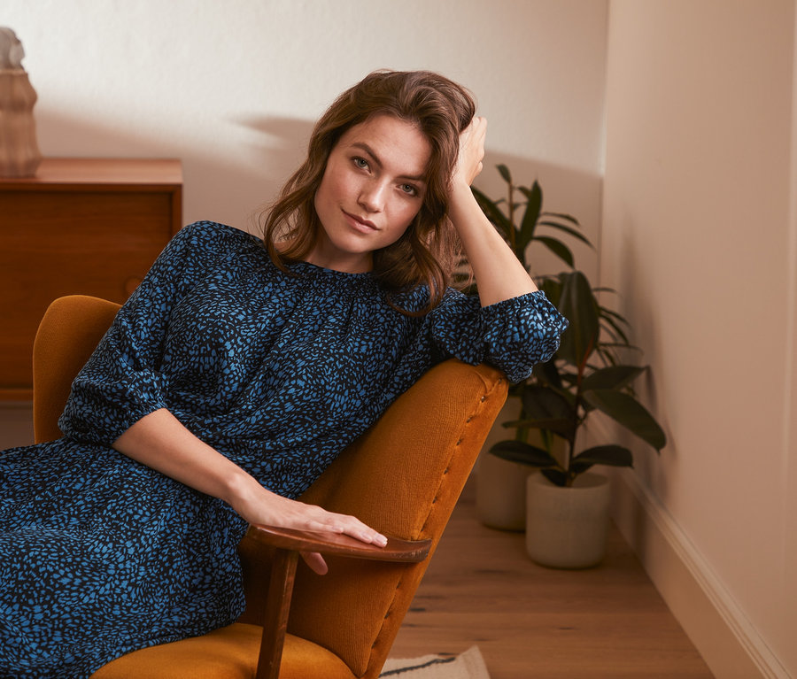 Frau sitzt im Sessel und trägt eine Bluse mit Print.