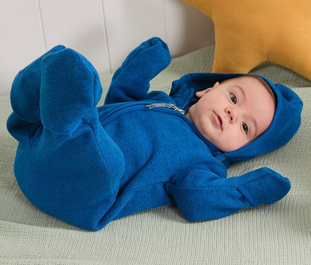 Ein Baby liegt auf dem Rücken in einem blauen Strickfleece-Einteiler mit Kapuze mit recyceltem Material.