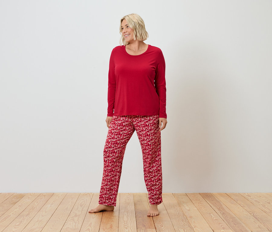Eine Frau mit blonden Haaren steht auf einem Holzboden und trägt einen roten Pyjama.
