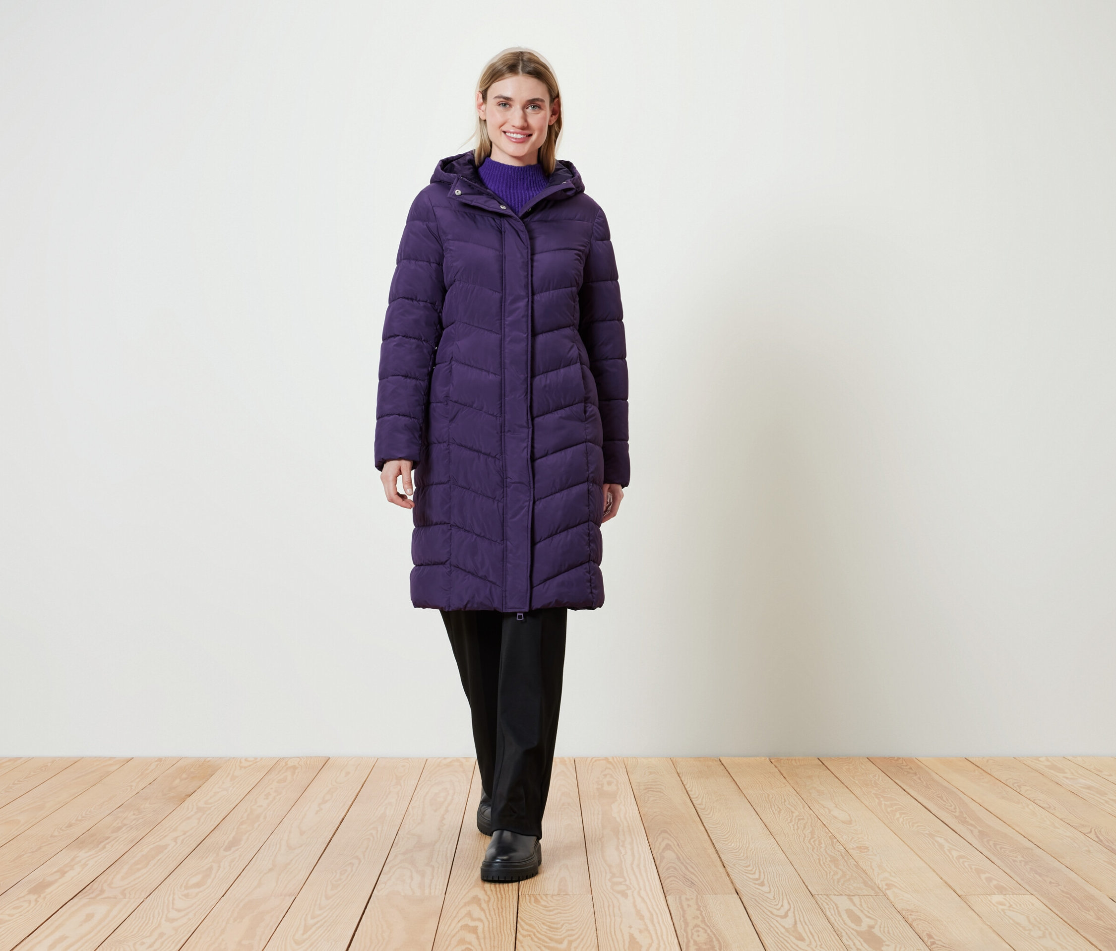 Frau trägt einen langen, lila Steppmantel mit Kapuze.