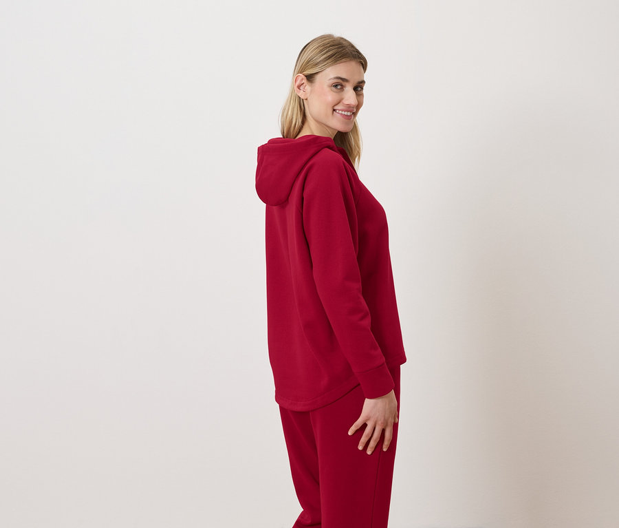 Frau im roten Hoodie-Anzug lächelt über die Schulter.