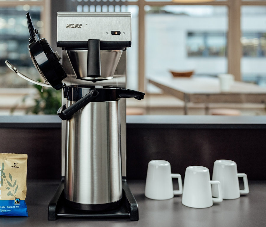 Auf einem Tisch stehen eine Profi-Filterkaffeemaschine »Bravilor-Bonamat TH« ohne Kanne, drei Tassen und eine Packung Kaffee.