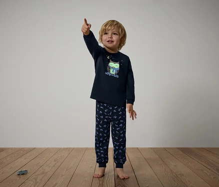 Junge im dunkelblauen Pyjama mit Eulenmuster zeigt mit dem Finger nach oben.