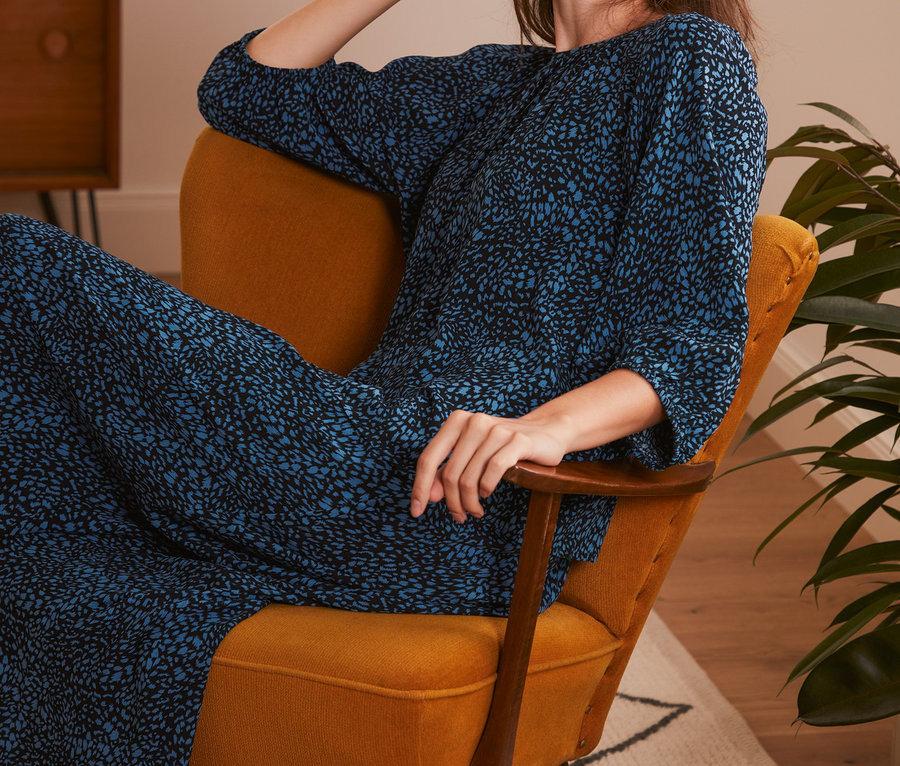 Frau sitzt im Sessel und trägt eine Bluse mit Print.