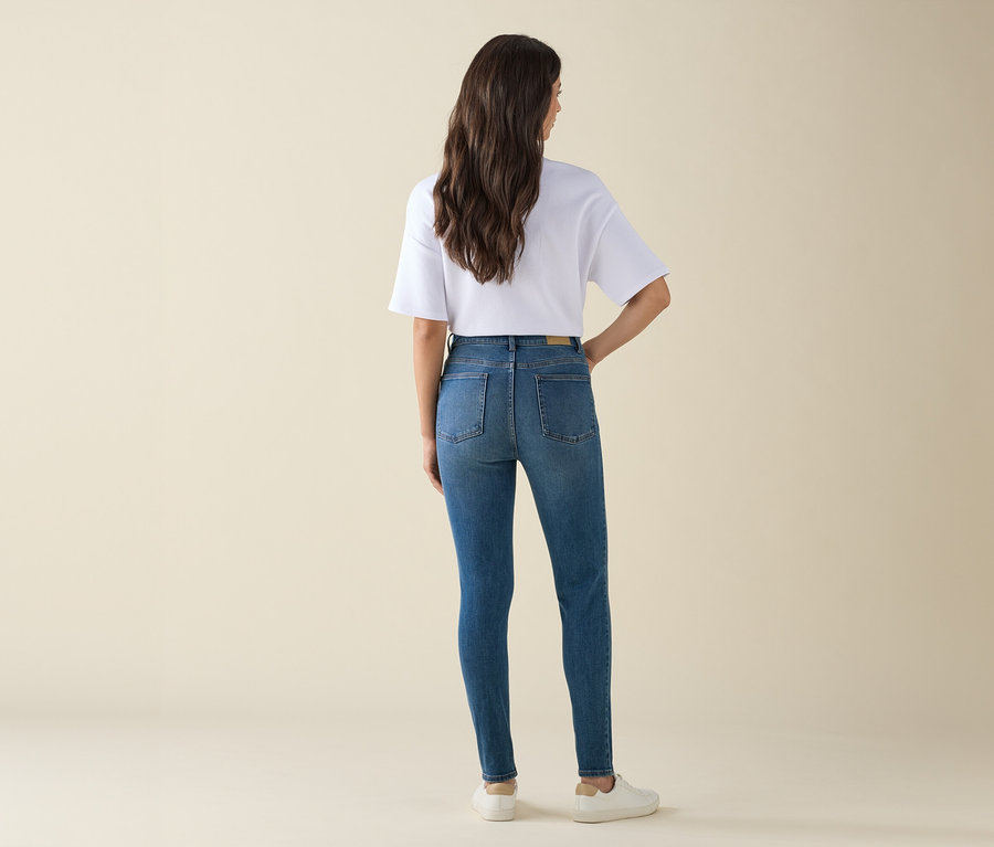 Rückansicht einer Frau mit braunen Haaren in blauen Jeans und einem weißen T-Shirt.