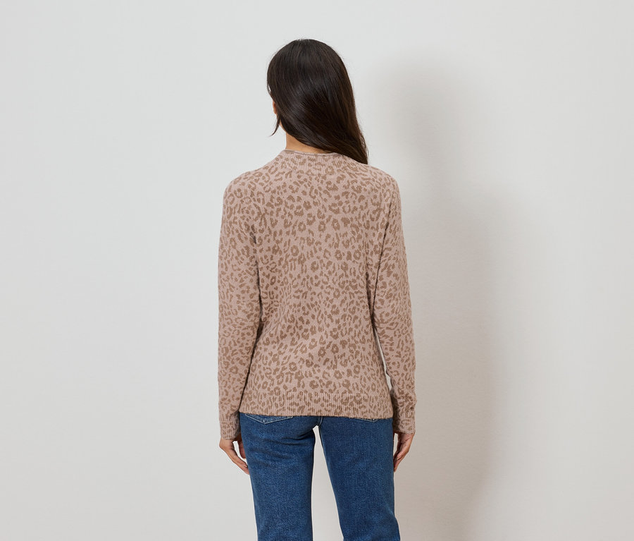 Rückansicht einer Frau mit langen dunklen Haaren, die einen hellbraunen Pullover mit Leopardenmuster und blaue Jeans trägt.