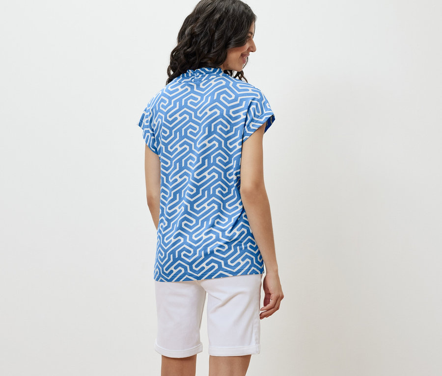 Frau trägt ein blaues Blusenshirt mit V-Ausschnitt und weiße Shorts.