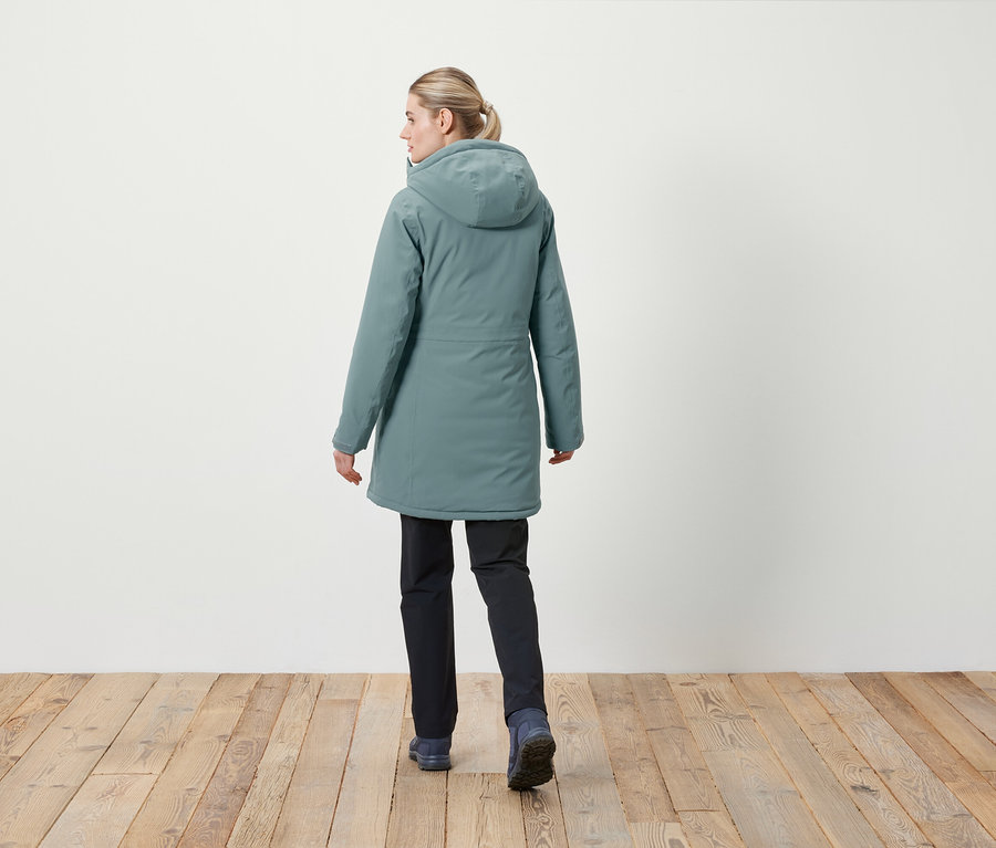 Frau mit dem Rücken zur Kamera trägt eine Jacke mit Kapuze und dunkle Hosen.