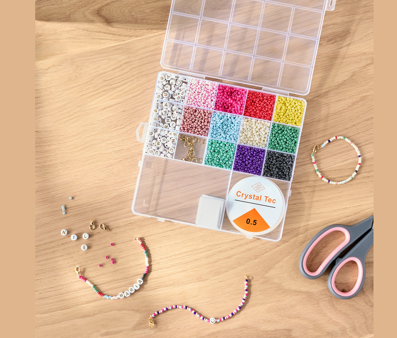 Geöffnetes DIY-Perlen-Set mit bunten Perlen, Schnur und Schere auf einem Holztisch.