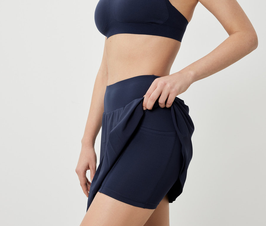 Frau posiert in Sport-BH und dunkelblauem Sportrock.