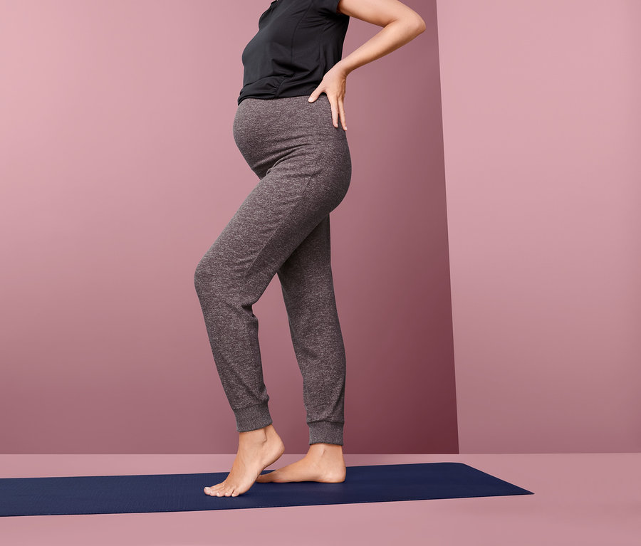 Schwangere Frau steht in Umstands-Relaxhose auf einer Matte.