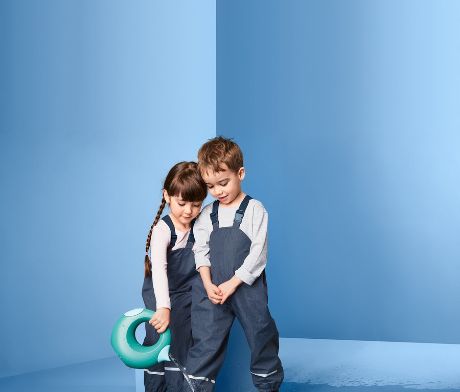Kinder in Regenhosen aus recyceltem Material spielen mit Wasser.