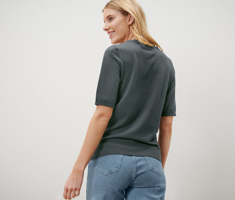 Eine Frau blickt über ihre Schulter und trägt einen grünen Feinstrickpullover und Jeans.