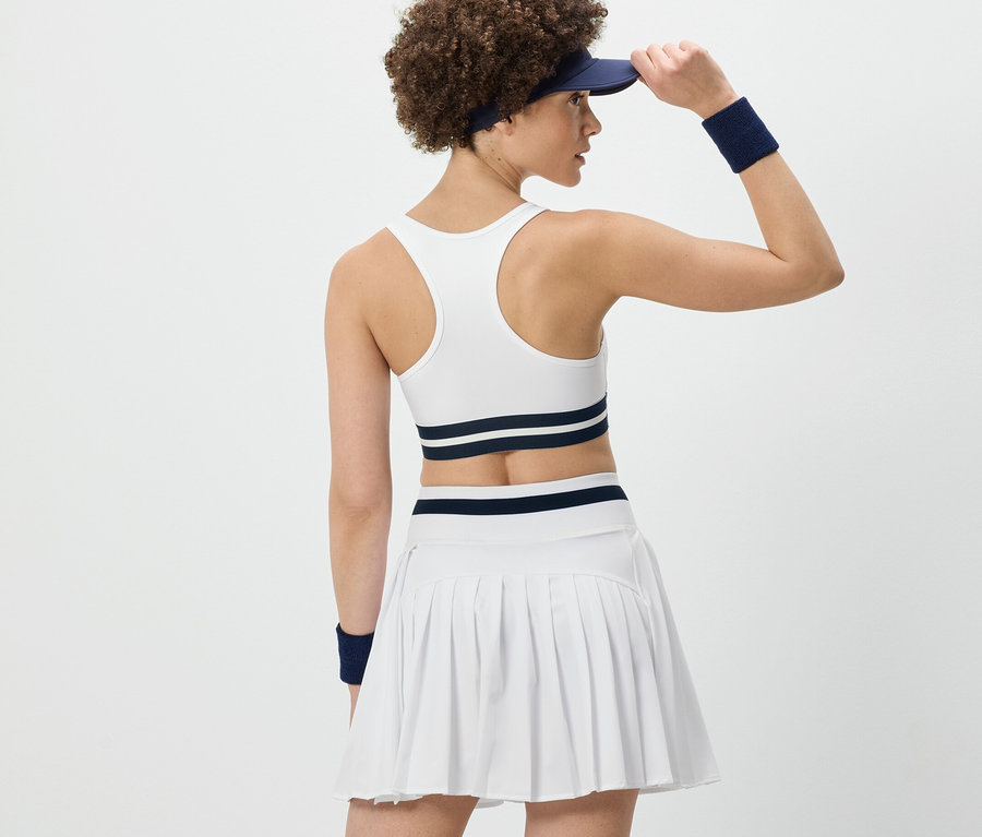 Frau von hinten, die ihr Visier richtet, trägt ein weißes Sport-Bustier »Crop Top« und einen weißen Faltenrock.