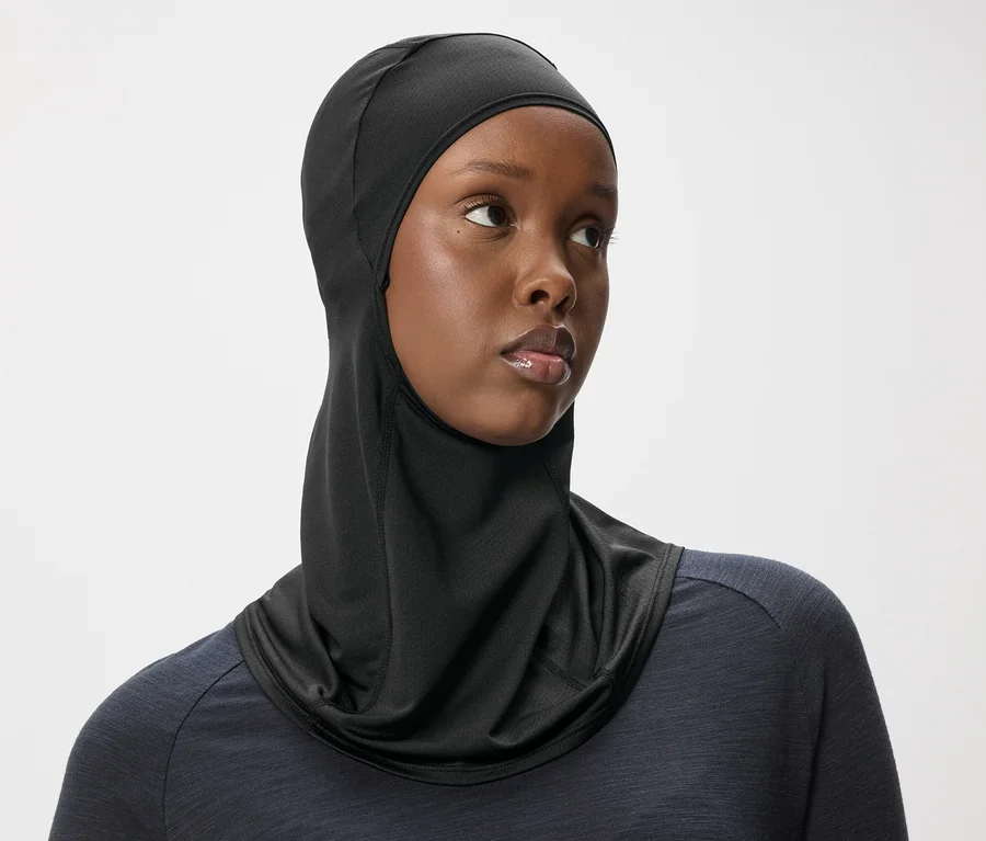 Frau mit dunkler Haut trägt ein schwarzes Hijab-Kopftuch und ein dunkles Oberteil vor einem weißen Hintergrund.