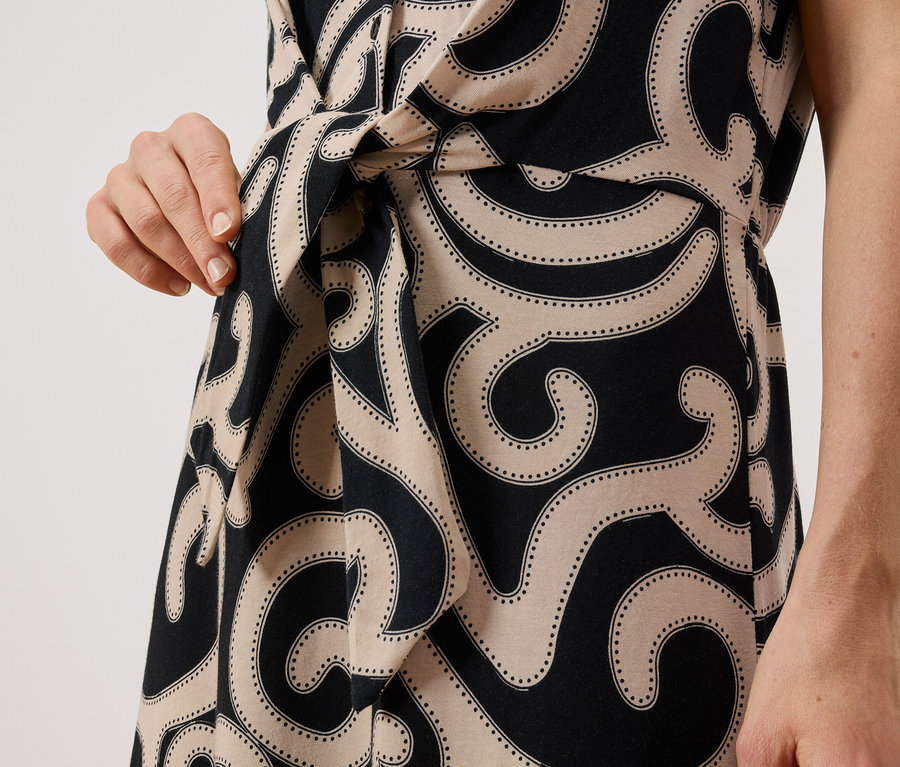 Nahaufnahme einer Frau, die ein gemustertes Kleid mit Wickel-Detail und einem gebundenen Gürtel trägt.