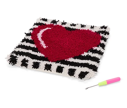 Quadratischer Teppich mit rotem Herz auf schwarz-weiß gestreiftem Hintergrund und Häkelnadel mit rosa-grünem Griff.
