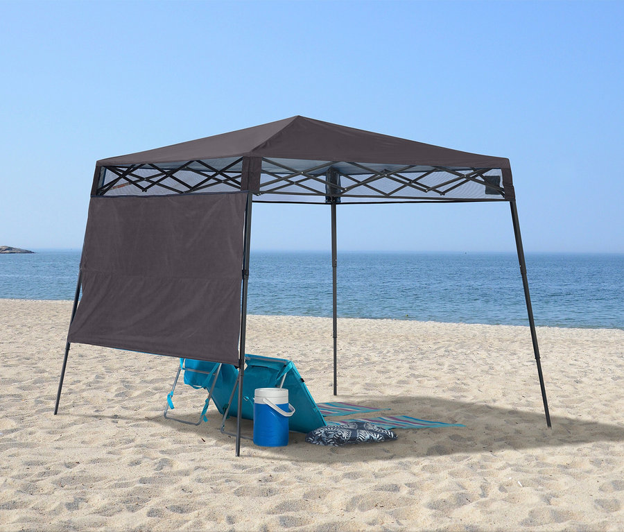 Am Strand steht ein grauer Pavillon mit einer blauen Strandliege, einer Kühlbox und einer Strandmatte darunter.