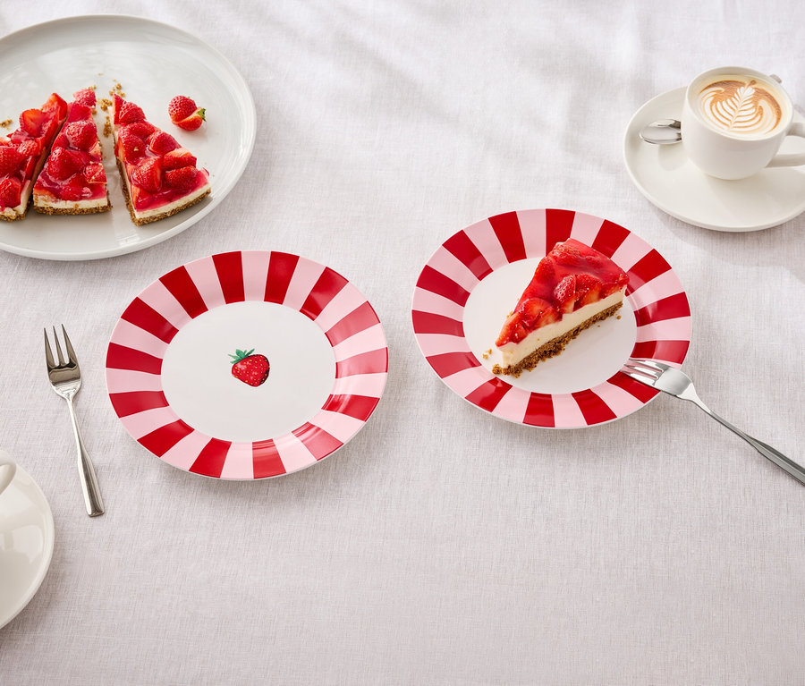 Auf einem Tisch liegen Teller mit Erdbeerkuchen, Gabeln und Tassen mit Latte Art.