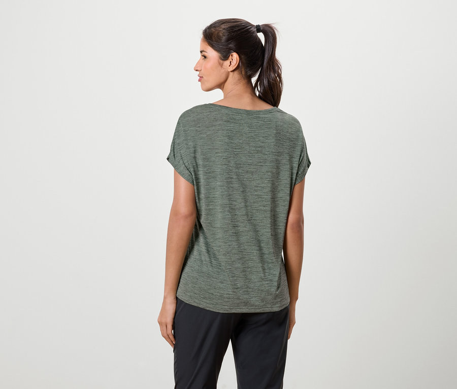 Eine Frau mit Pferdeschwanz trägt ein grünes T-Shirt und schwarze Hosen.