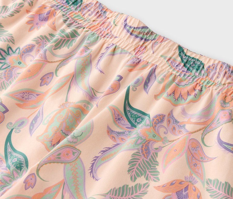 Nahaufnahme eines hellpfirsichfarbenen Stoffes mit einem Muster aus Blumen und Blättern in Grün-, Lila- und Pfirsichtönen.